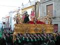 Procesión religiosa con hermandad portando un paso ornado con oro y una imagen de la Virgen en un entorno urbano.