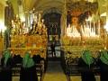 Una iglesia con altares dorados y velas encendidas, adornos religiosos y una figura central.
