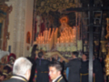 Imagen de una procesión religiosa en un templo, con personas vestidas formalmente y velas encendidas.