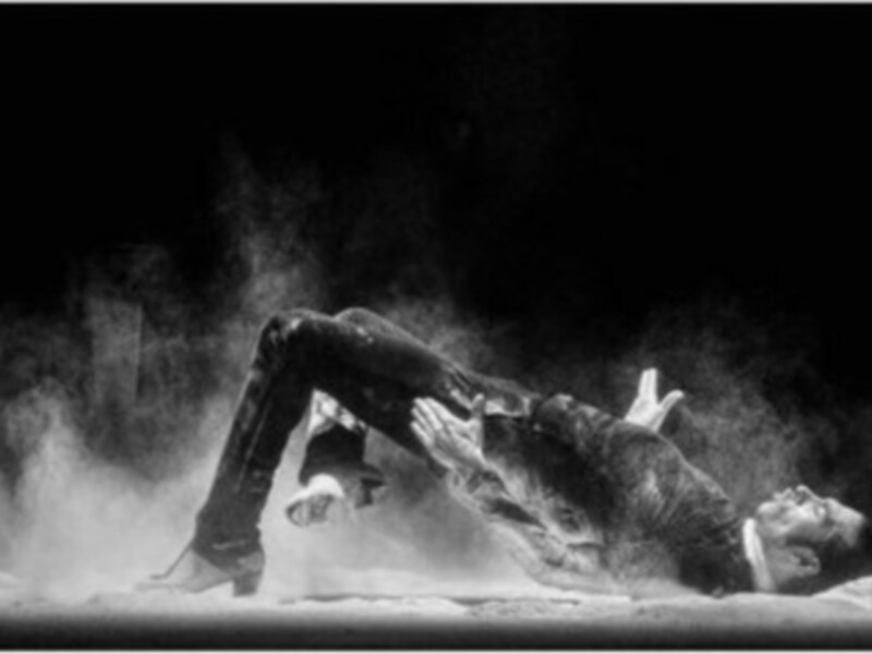 Danza contemporánea en blanco y negro, con polvo en el aire y una postura dinámica en el suelo.