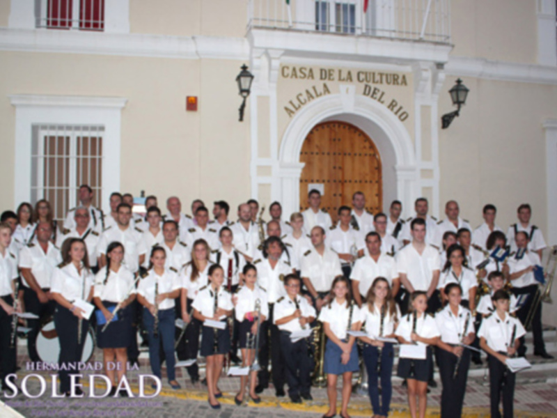 Fotografía de una gran agrupación de personas vestidas en uniforme blanco y negro, posando frente a la Casa de la Cultura Alcalá del Río. La imagen muestra una celebración o evento formal en un entorno histórico con elementos arquitectónicos y decorativos.