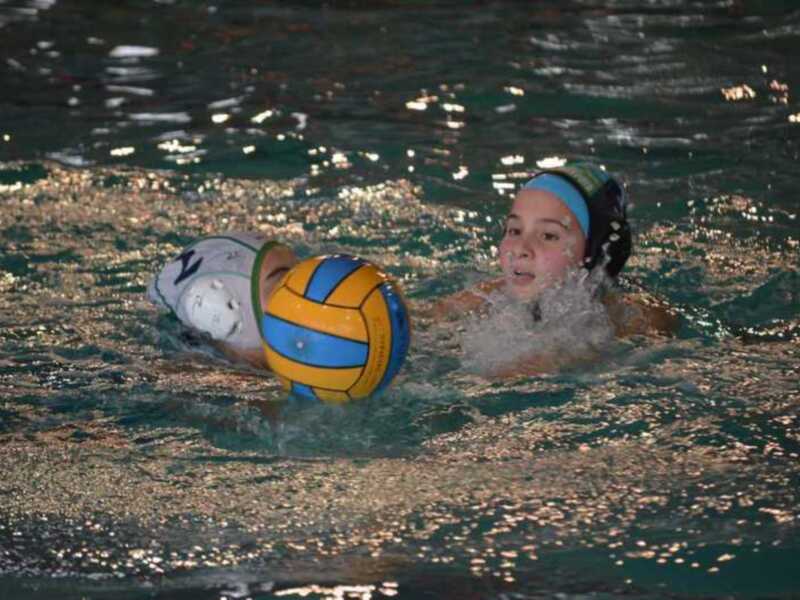 Una niña está jugando voleibol de agua en un estanque nocturno. La imagen muestra a la niña con una pelota de voleibol de agua, posiblemente en un partido o entrenamiento nocturno.