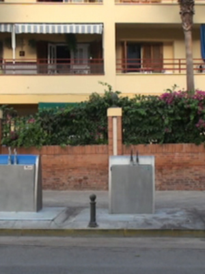 Se muestra una calle con dos casas de apartamentos amarillas, un toldo en la parte superior y un parque con flores. También se pueden ver dos estaciones de lavado de autos en el lado izquierdo y un toldo amarillo en la parte superior derecha.