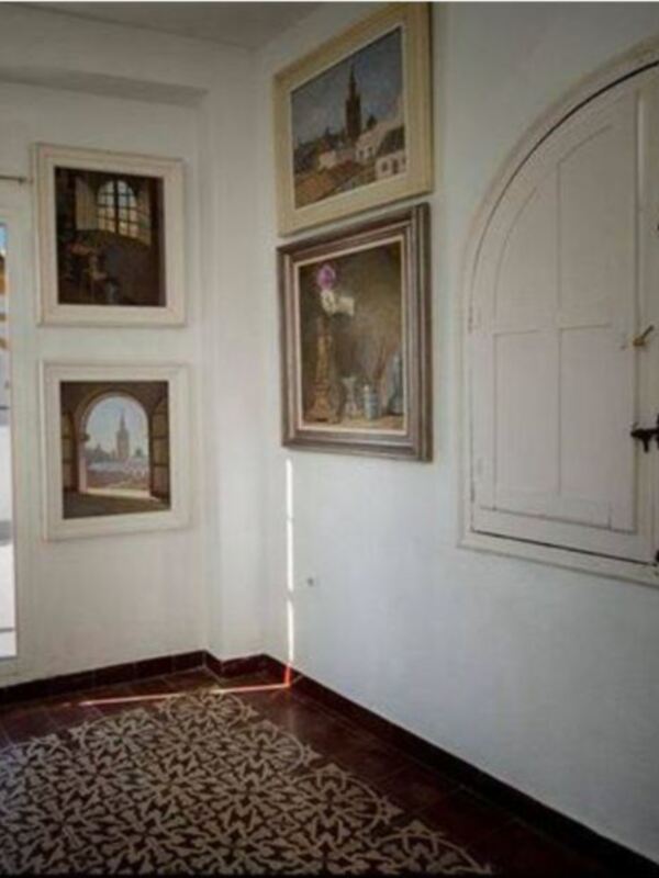 Salón con ventana que refleja la Catedral de Sevilla y cuadros sobre el tema. Piso con alfombra de diseño.