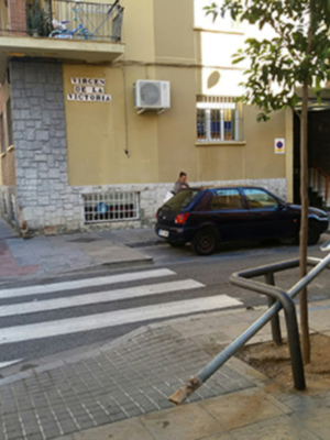 Calle con peatonal, coche estacionado y edificio con balcones.