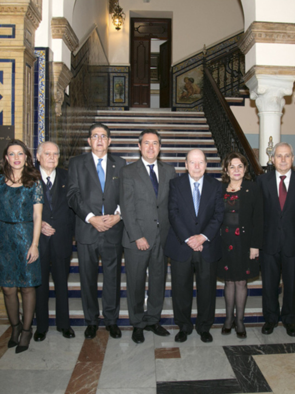 Una imagen de una fila de siete personas posando frente a una escalera decorada con azulejos y molduras. La escena parece ser formal, posiblemente en un evento o reunión oficial.