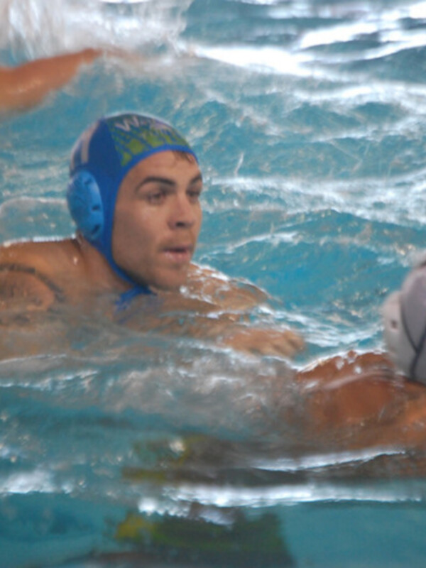 Juego de waterpolo en una piscina con dos jugadores, uno con el número 7 en la camiseta y otro con el número 10 en la camiseta, ambos con cascos azules y nadando en el agua azul claro.