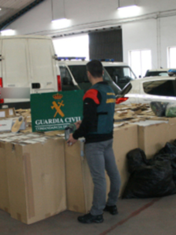 Operación de la Guardia Civil con vehículos y cajas de evidencias en un almacén.