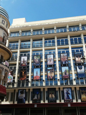 Edificio histórico con arcos y balcones, decorado con grandes carteles de películas. Sobre un cielo azul claro.
