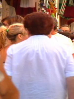 Una multitud de personas caminando en una calle, con tiendas y colores en el fondo.
