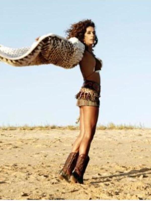 Una mujer en una playa desierta con un mantón de plumas volando alrededor de ella.