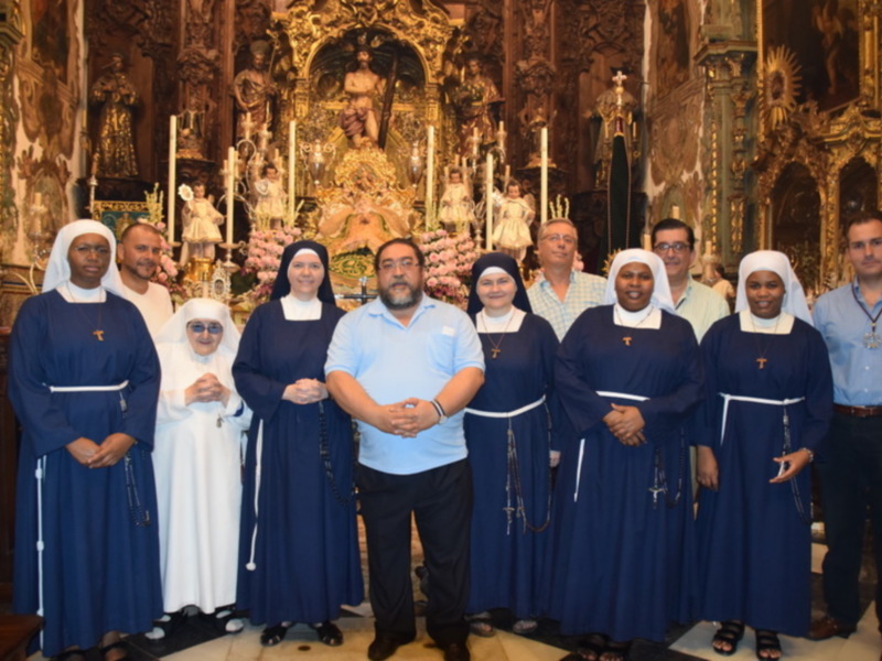 Una imagen de una reunión en una iglesia, con religiosos y religiosas posando frente a un altar con estatuas y velas.