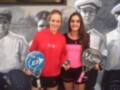 Dos jóvenes mujeres posan con raquetas de pádel en un entorno deportivo, con un mural de jugadores de tenis en el fondo.