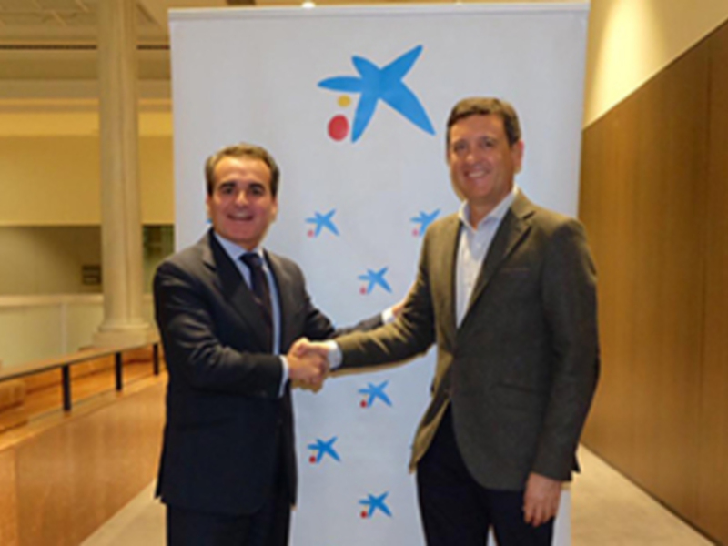 Dos hombres en trajes se saludan frente a un fondo con el logo de Xataka.