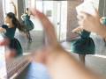 Una niña baila en un vestido verde, frente a espejos que reflejan su figura. Detalles como el suelo de madera y la cortina de bambú contribuyen al ambiente de estudio.