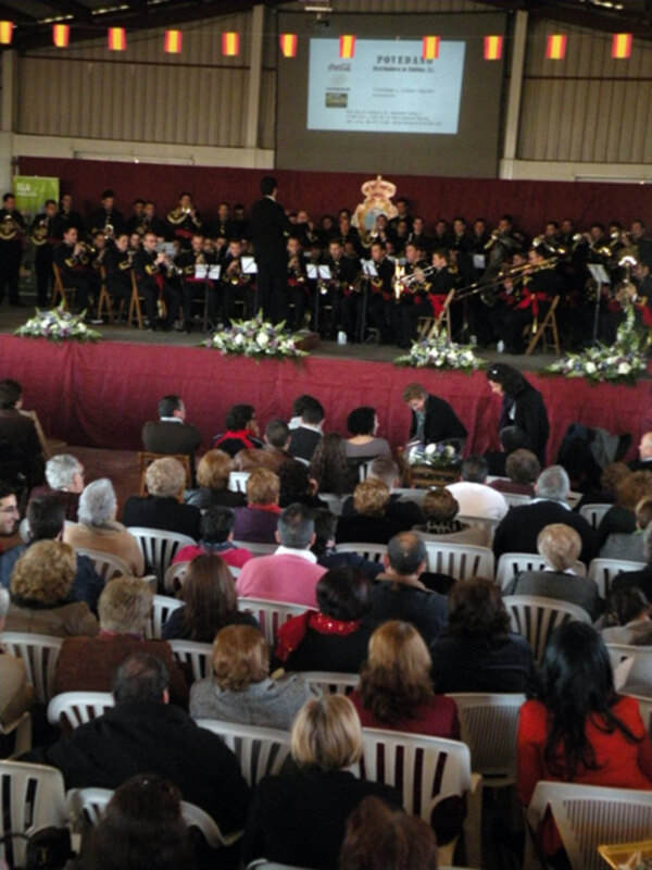 Concierto de banda en una sala con público asistiendo y orquesta tocando.