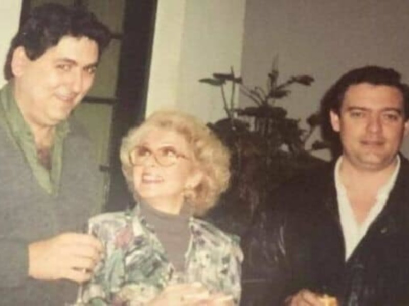 Una imagen de tres personas posando juntas, dos hombres y una mujer mayor con gafas. La escena parece ser en un ambiente interior, posiblemente una fiesta o reunión familiar.