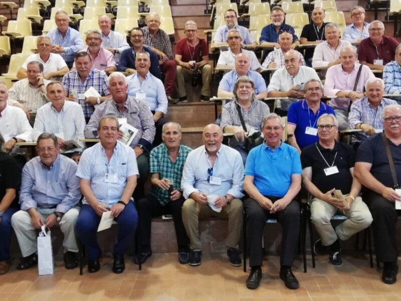 Grupo de personas sentadas en una sala de conferencias, posiblemente en un evento o reunión. Todos parecen estar atentos a algo, posiblemente una presentación o charla. La sala está llena de asientos vacíos, lo que sugiere que el evento es bien recibido o que la audiencia está limitada.