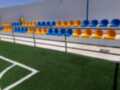 Sala de espera para jugadores con sillas azules y amarillas, ubicada cerca del campo de fútbol artificial.