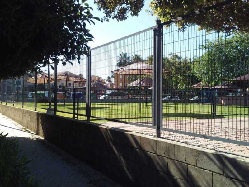 Fence with trees and buildings in the background.