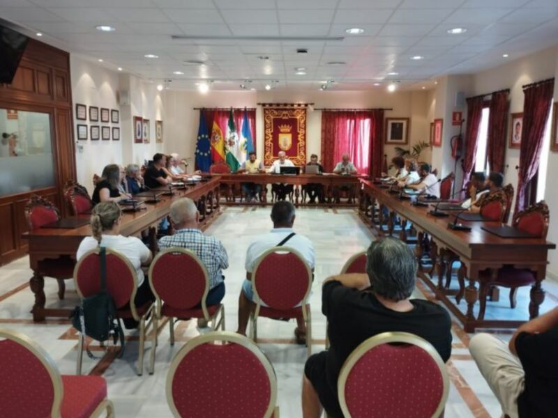 Reunión de trabajo en una sala de conferencias con banderas y escudo de armas en el fondo.