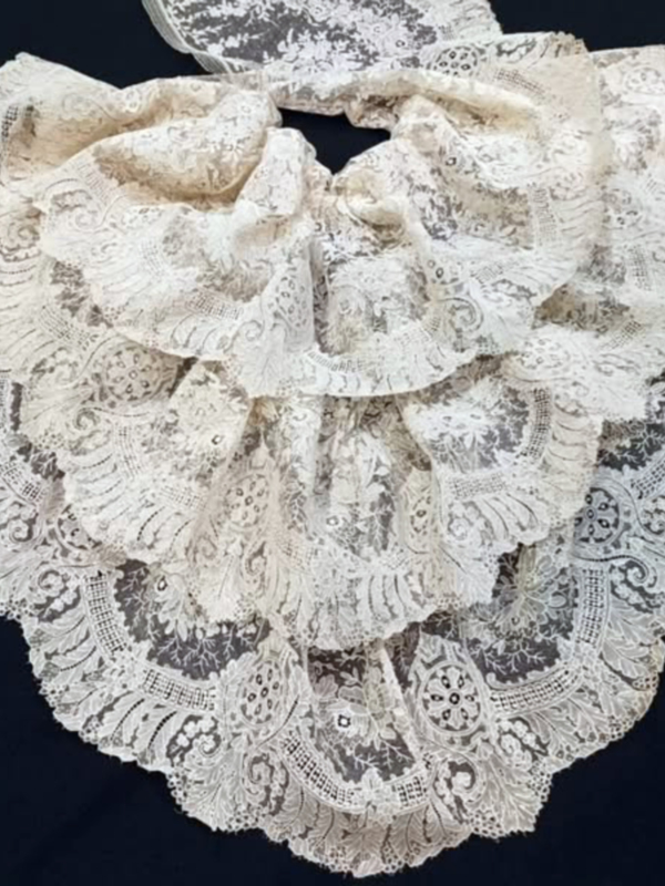 Lámina de encaje blanco con detalles bordados y volantes, fondo negro.