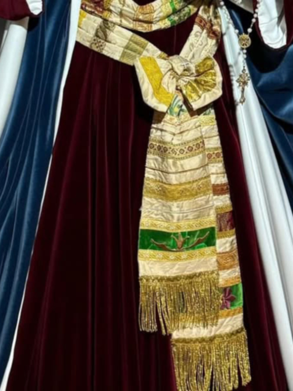 Una imagen detallada de un vestido ceremonial con una capa roja, un pañuelo dorado y una corona.