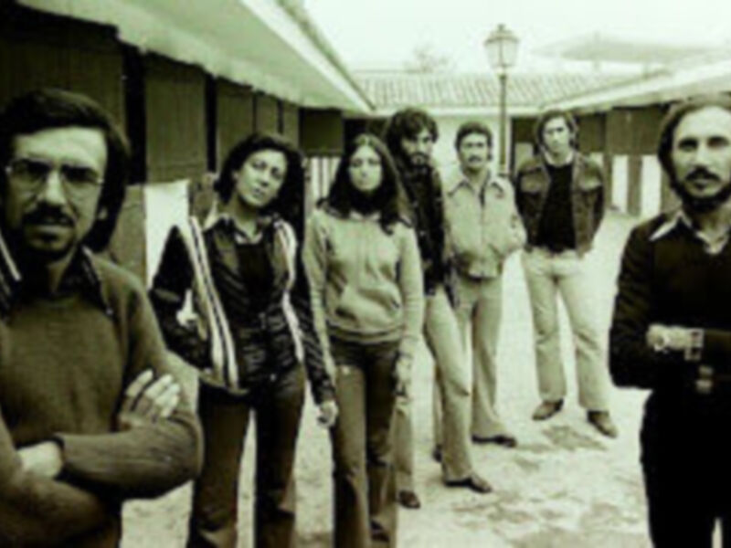 Una foto en blanco y negro de un grupo de personas posando juntas, incluyendo a una mujer con una chaqueta y pantalones de cuadros.