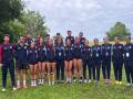 Equipo de atletas posando en un campo verde, con uniformes azules y rojos, y medallas en el cuello.