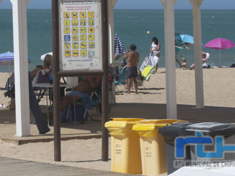 Pérgola en la playa con carteles informativos y personas disfrutando del sol.