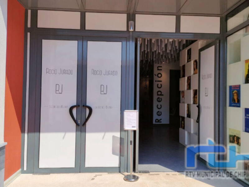 Puerta de acceso a la recepción con un letrero que dice "Recepción". La entrada está decorada con carteles y fotos de personas.