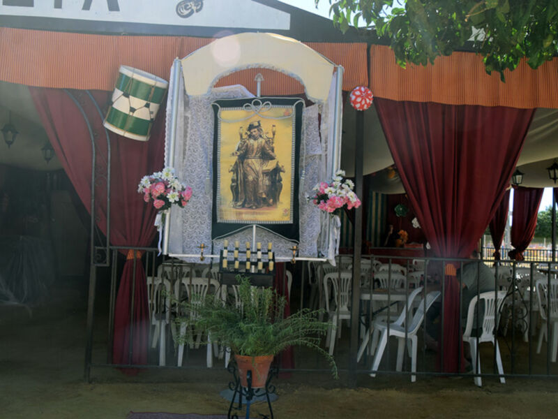 Una imagen de una iglesia con un altar adornado con flores y velas, rodeada por cortinas rojas y una gran lámpara de techo.