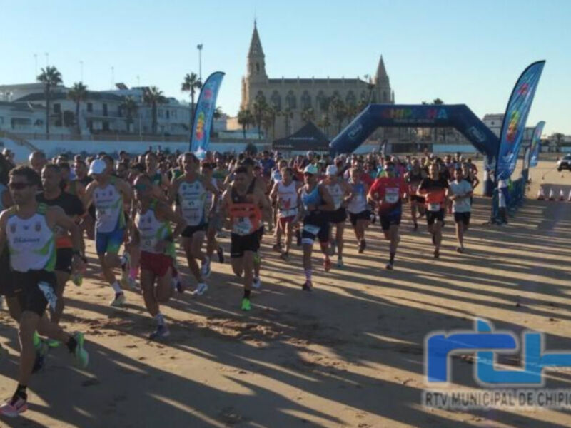 Corredores en la línea de salida de una maratón costera, con el mar y la ciudad al fondo.