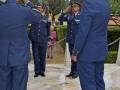 Un grupo de oficiales militares en uniforme azul saludan a una mujer anciana con un ramo de flores, todo en un entorno formal y ceremonial.