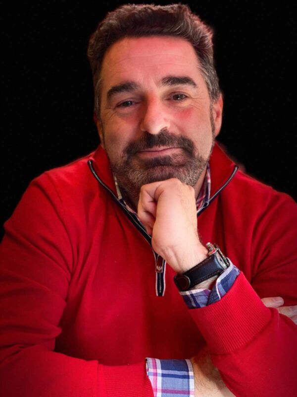 Un hombre con una camisa roja y un reloj en la muñeca, posando contra un fondo negro.