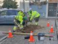 Trabajadores en uniforme amarillo trabajando en un agujero en el pavimento, rodeados de conos de seguridad y herramientas.